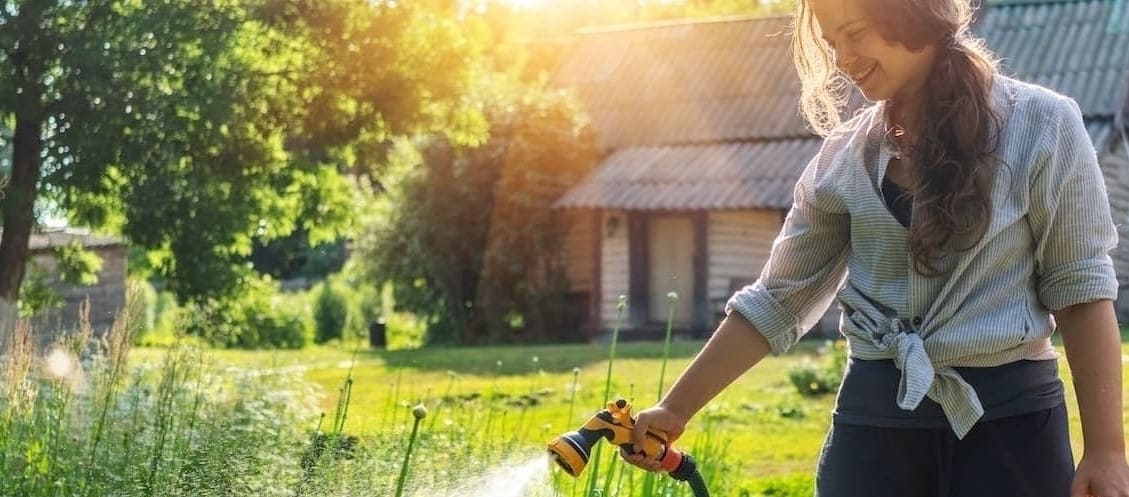 Woman Watering Garden On Rural Home Lawn