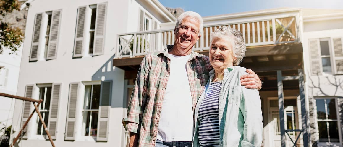 Older wife and husband outside their home.