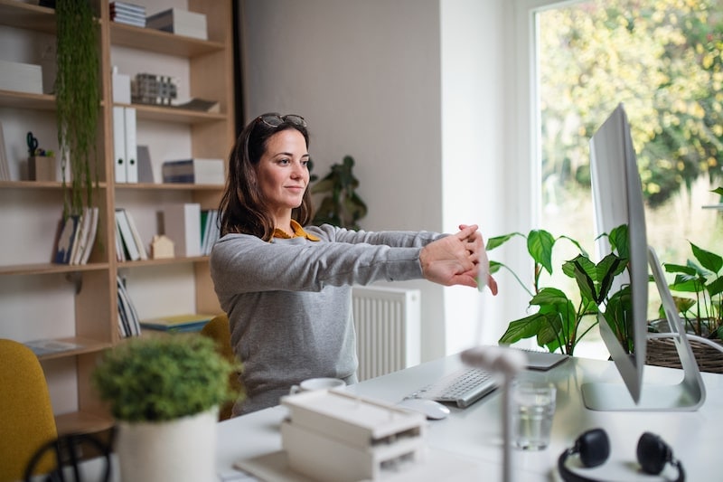 Woman stretching at home office desk.