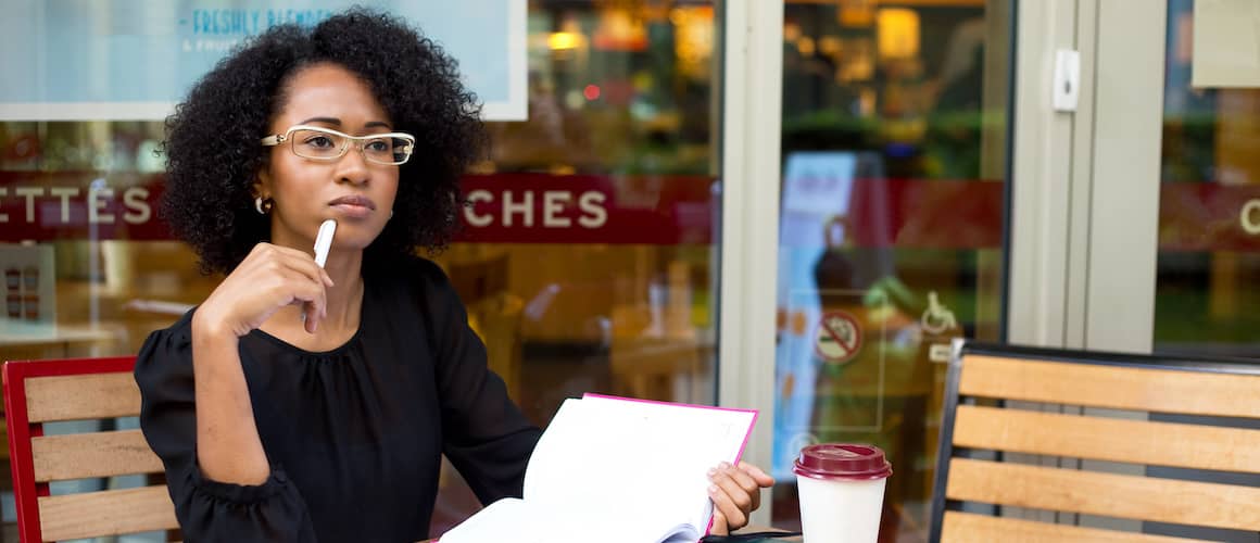 A woman looking thoughtful with papers sitting outside a coffee shop.