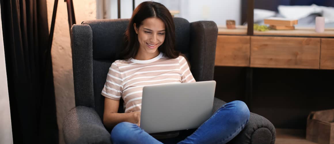 Woman Sitting In Denim Chair Working On Laptop