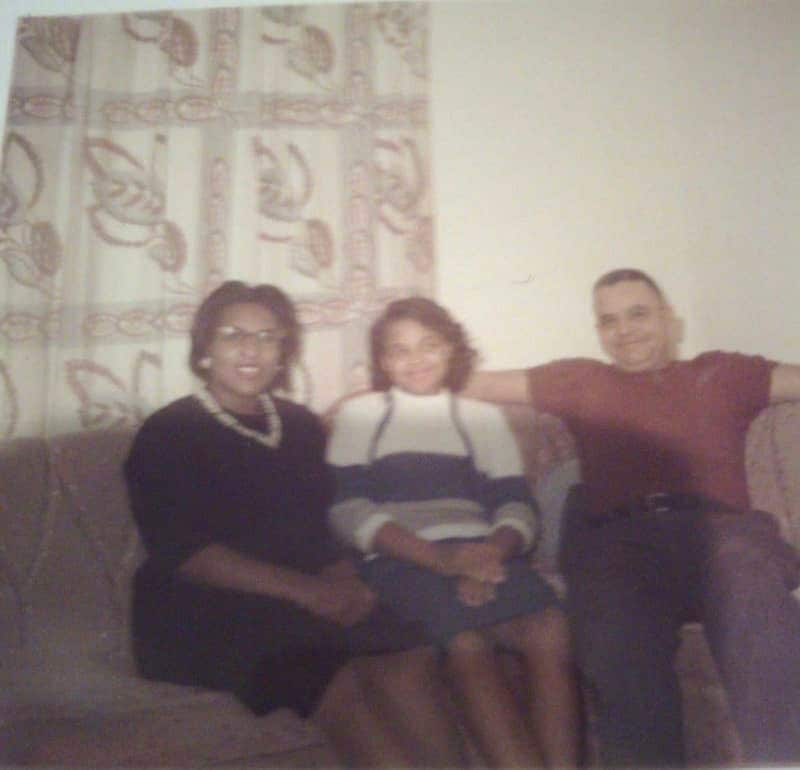 Picture of young Esther between her parents on sofa.