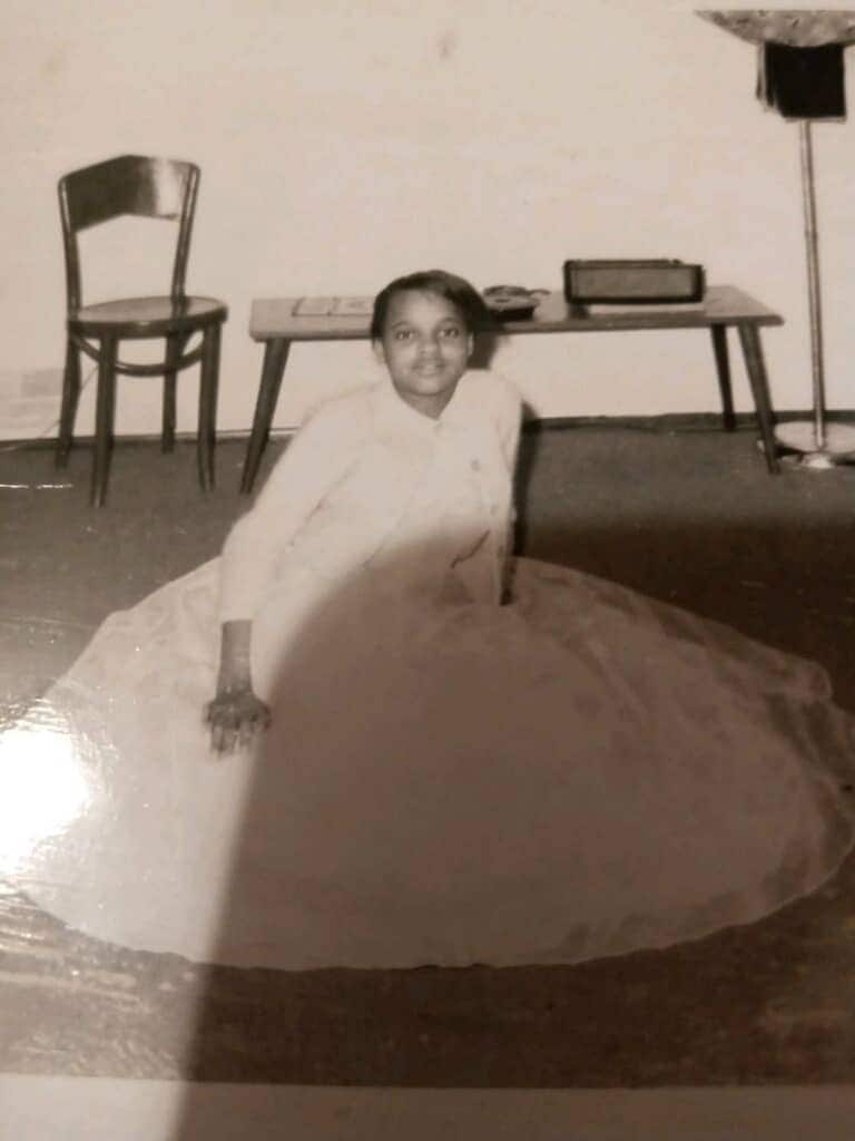 Black and white photo of Esther sitting on the ground in a dress.