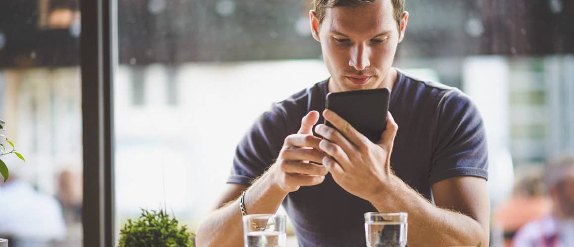 Man at cafe on phone looking at app.