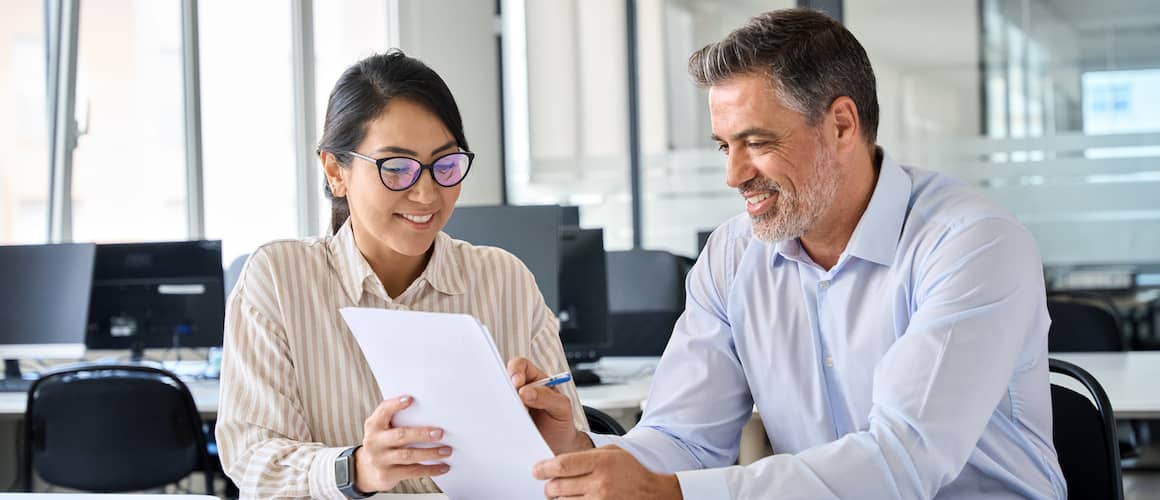 Professional woman holding up paperwork to man as he reads and signs it.