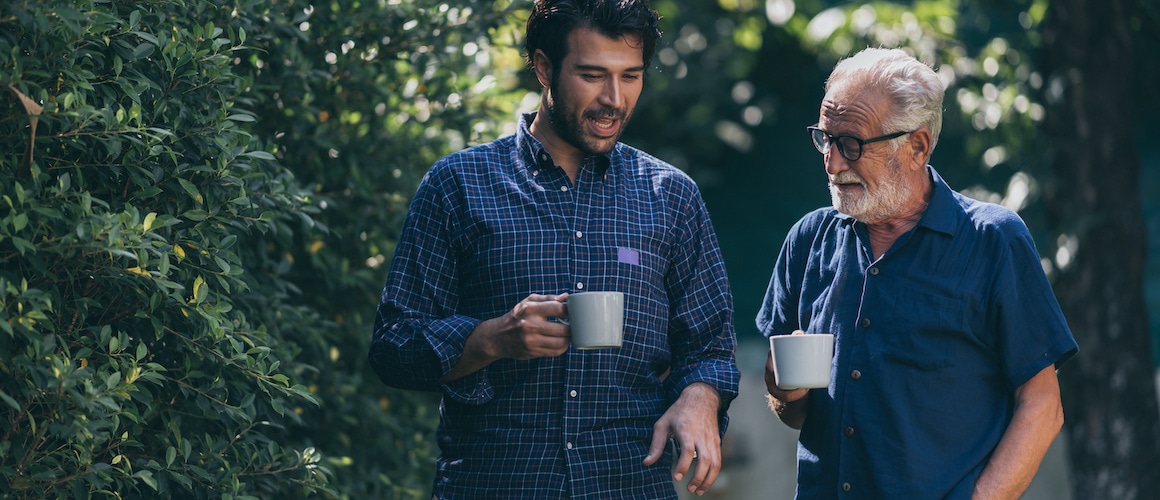 Adult Son And Senior Father Talking With A Cup In Their Hands