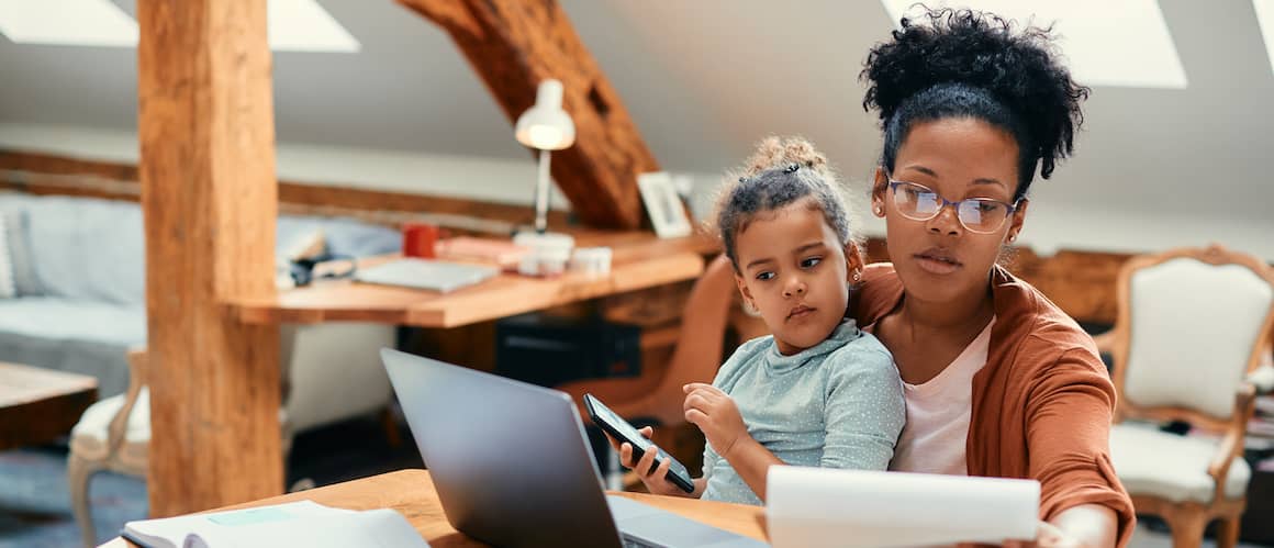 African-American mother works on finances with toddler daughter in her lap.