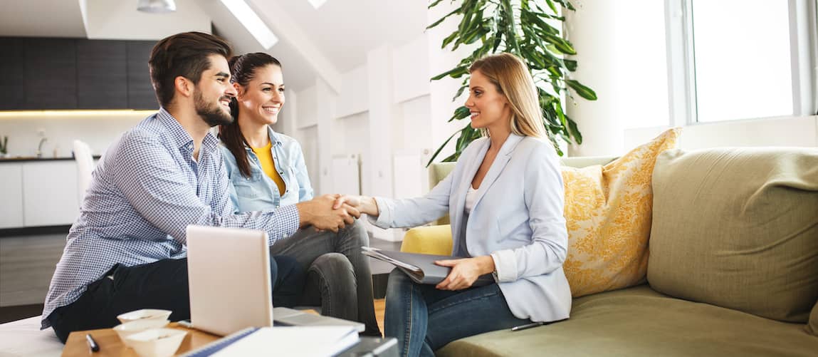 Real estate agent agent shakes hands with couple after signing documents.