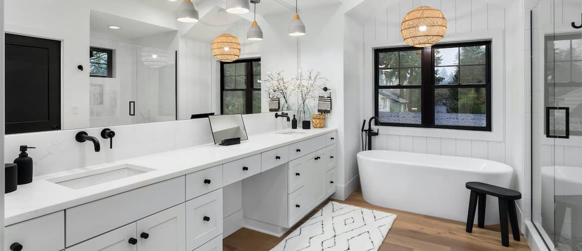 Renovated modern black and white bathroom with boho style lighting over tub.