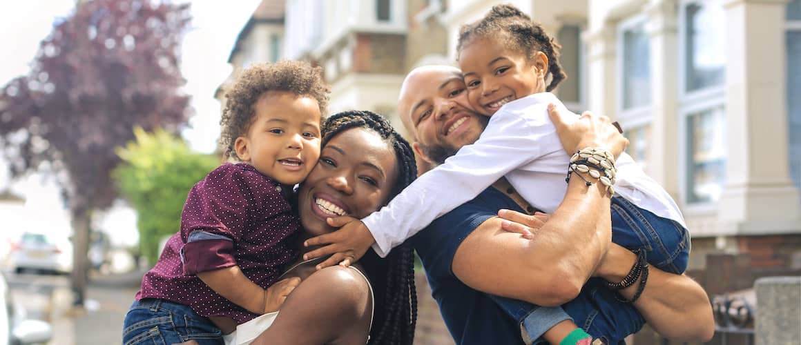 Black family of four embracing outside home in group photo.