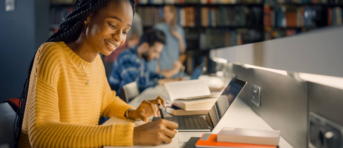 Black Woman In A Yellow Sweater Writes Notes In A Library