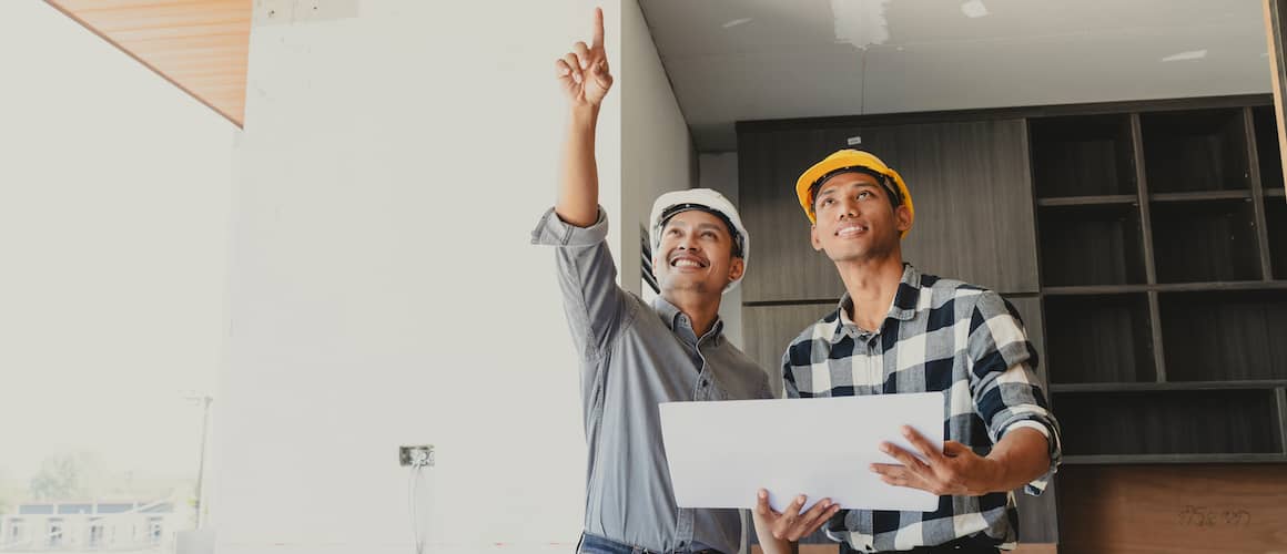Contractors Holding Large House Blueprints In Newly Built Construction