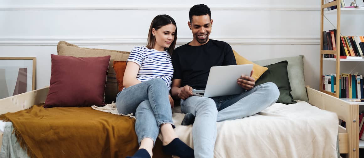 Couple snuggling on pullout couch and looking at laptop together.