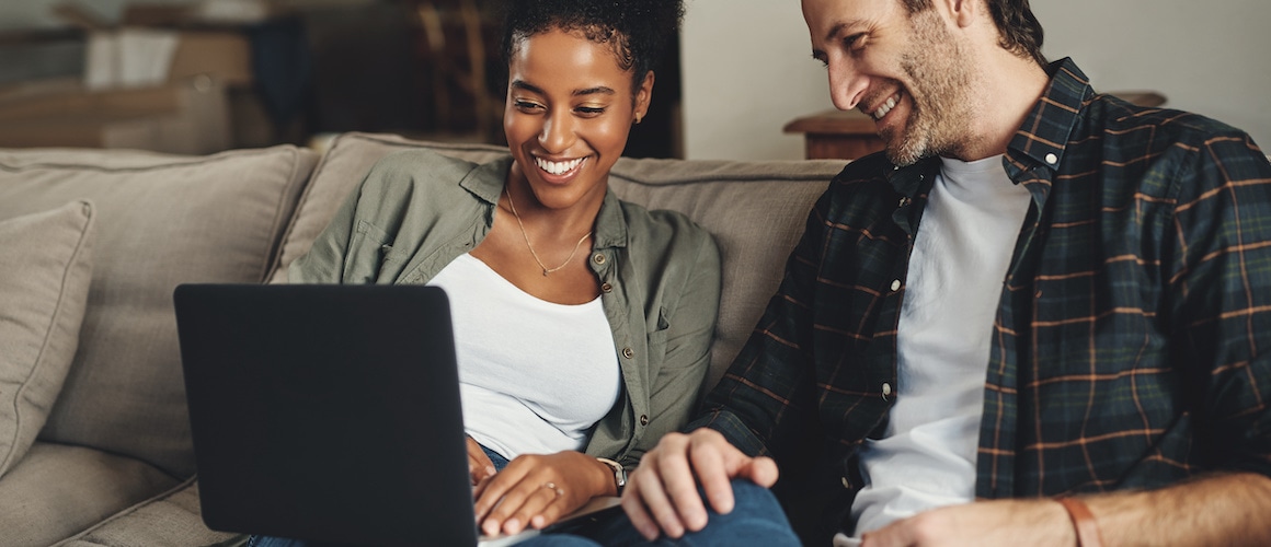 Couple smiling on couch looking at laptop together.