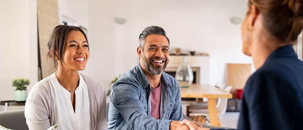 Couple sitting on a couch shakes hands with a real estate agent