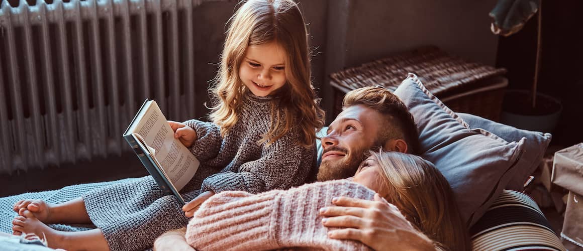 Dad with mom and daughter reading a book and cuddling.