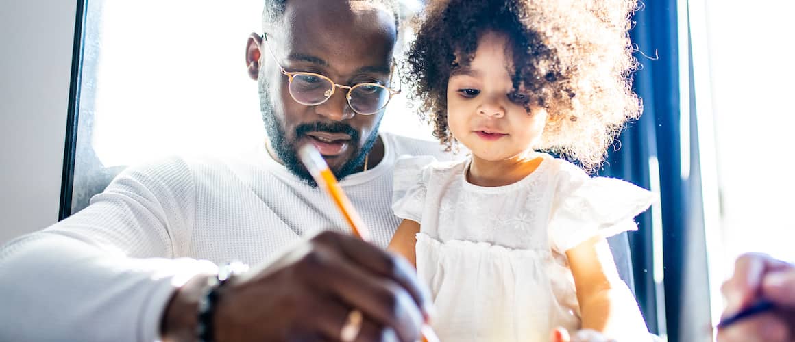 Father with young daughter working on drawing with a pencil.