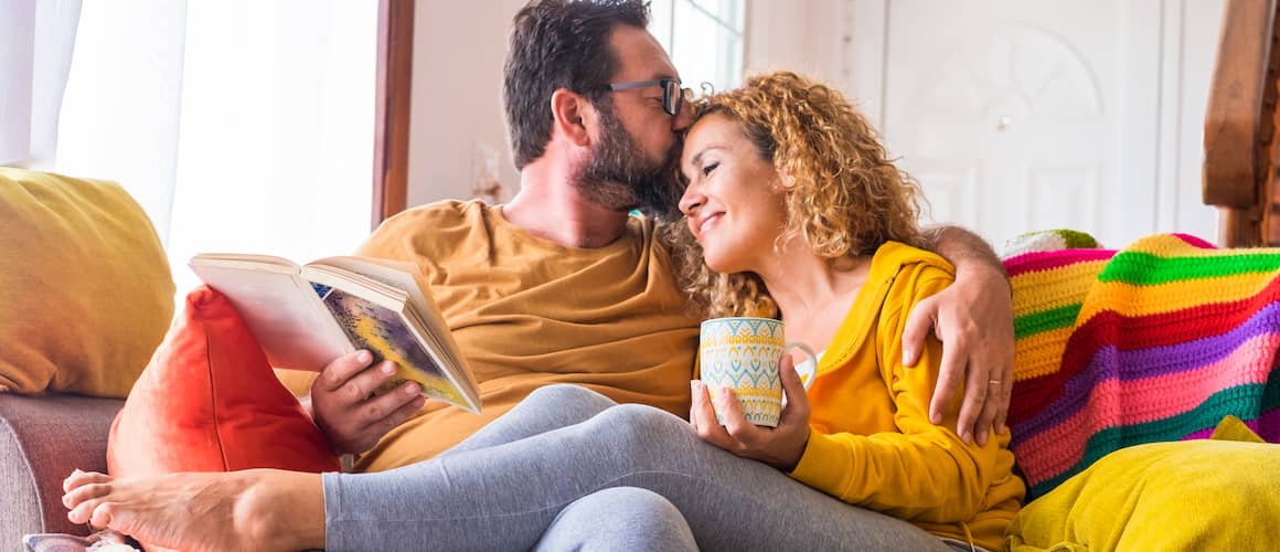 Young happy couple on the couch together reading and drinking coffee.