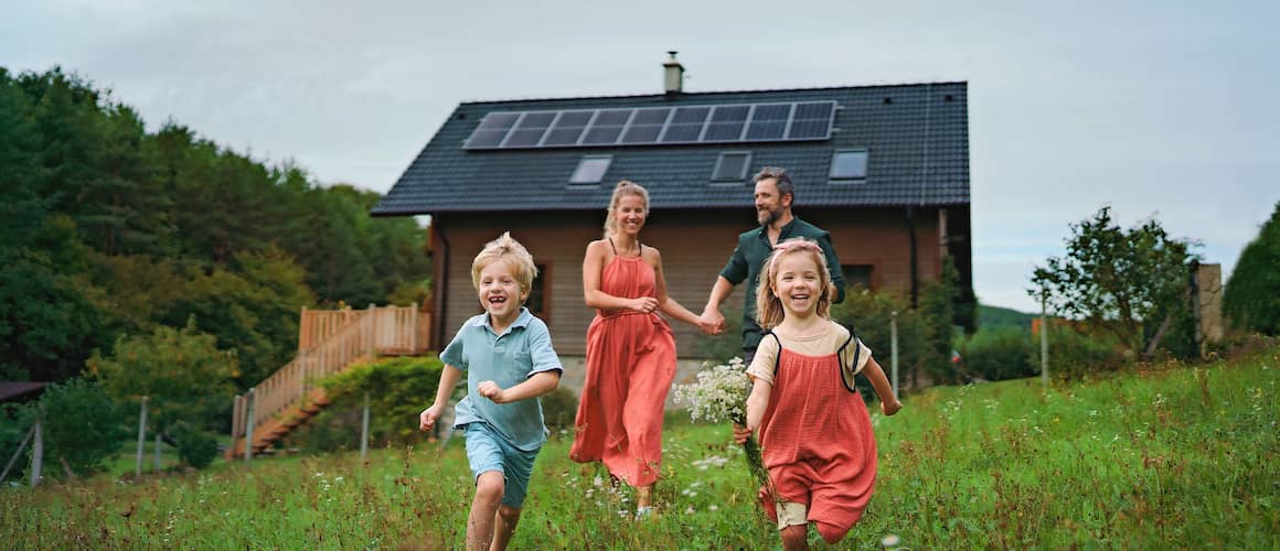Happy family of four running towards camera and away from house with solar panels on the roof.