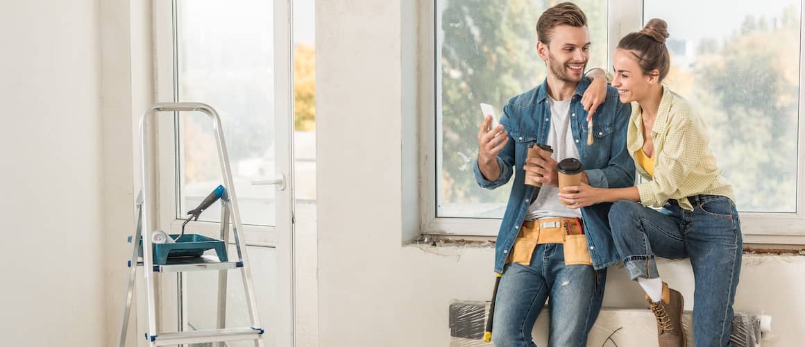 Happy Young Couple Holding Paper Cups And Looking At Smartphone