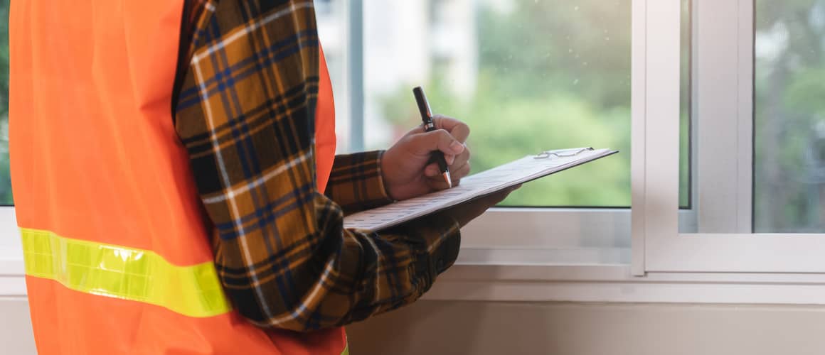 Home inspector holding a clipboard and standing in front of a window.