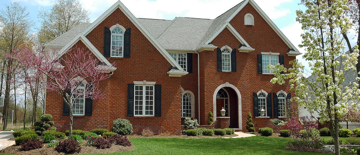 Large red brick multi-story home with a large front yard including flora.