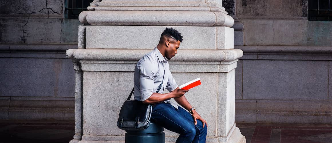 Man reading a book sitting on a pillar.
