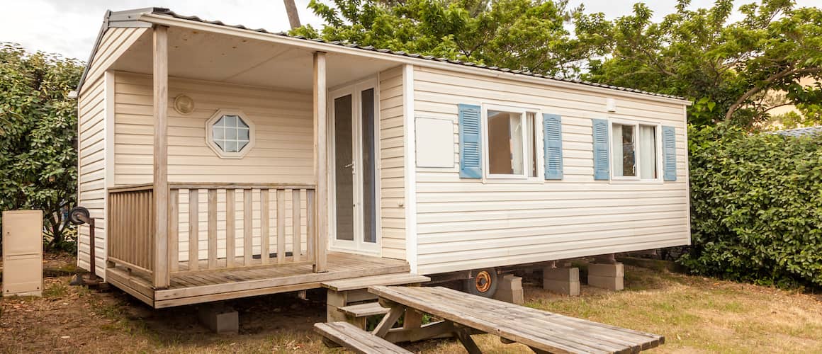 Beige mobile home at a camping site with a picnic table outside.