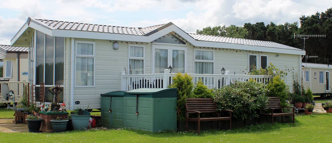 Modern mobile home with benches and potted plants outside.