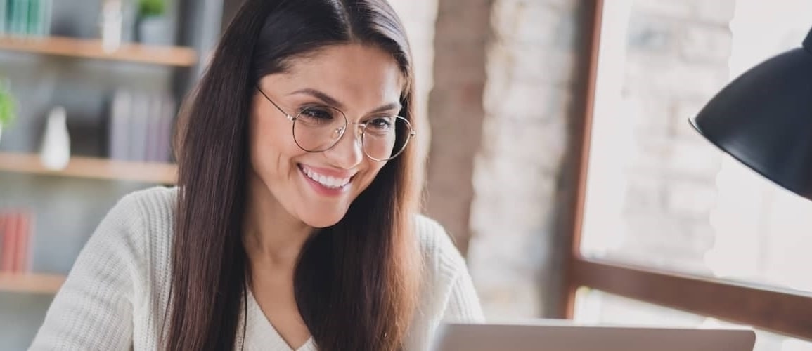 Woman with long brown hair smiling at laptop.