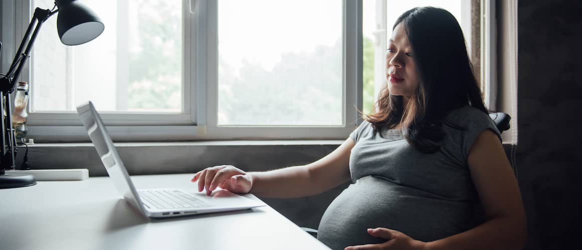 Pregnant Asian woman browses the internet on computer.