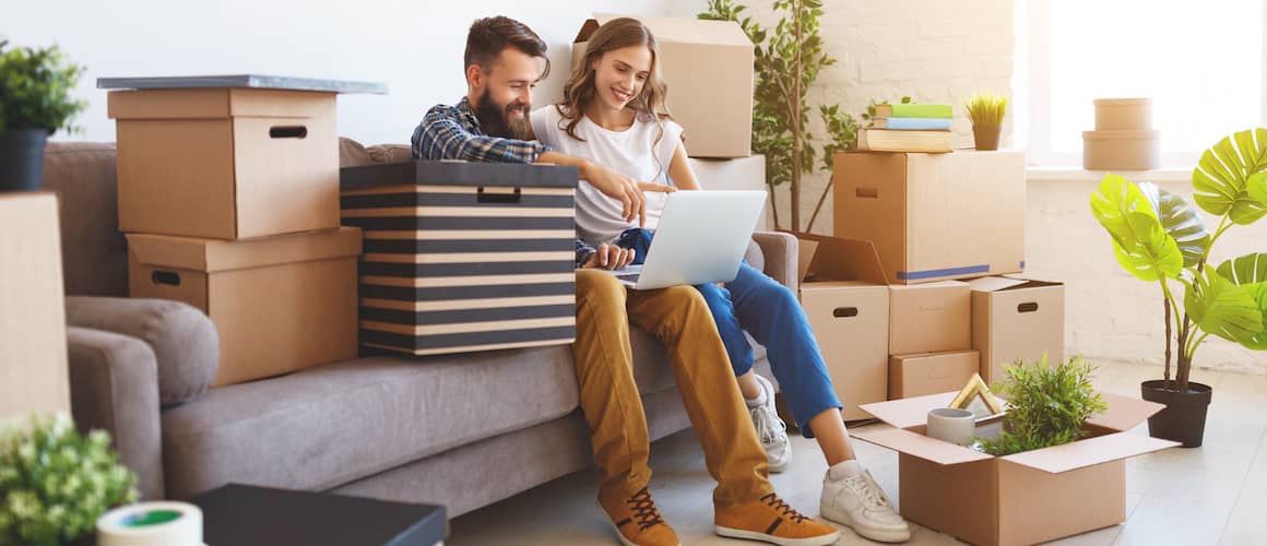 Young couple reviewing RateShield info online on couch amongst partially unpacked boxes in new home.