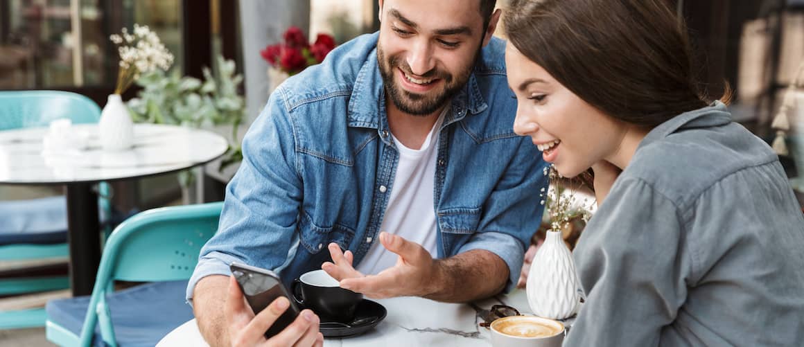 Couple excitedly looking at homes for sale online at cafe.