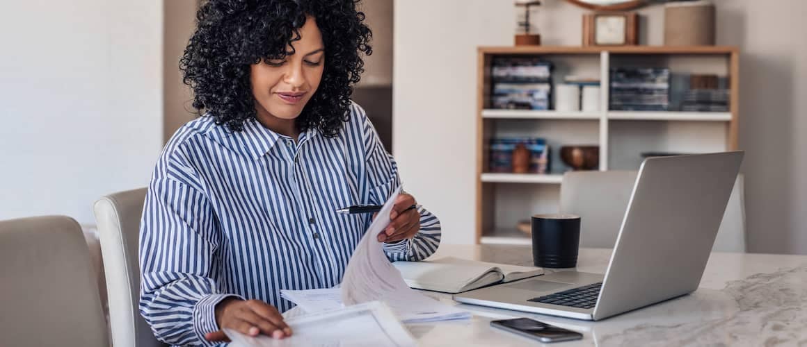 Smiling Female Entrepreneur Going Through Paperwork At Her Dining Table