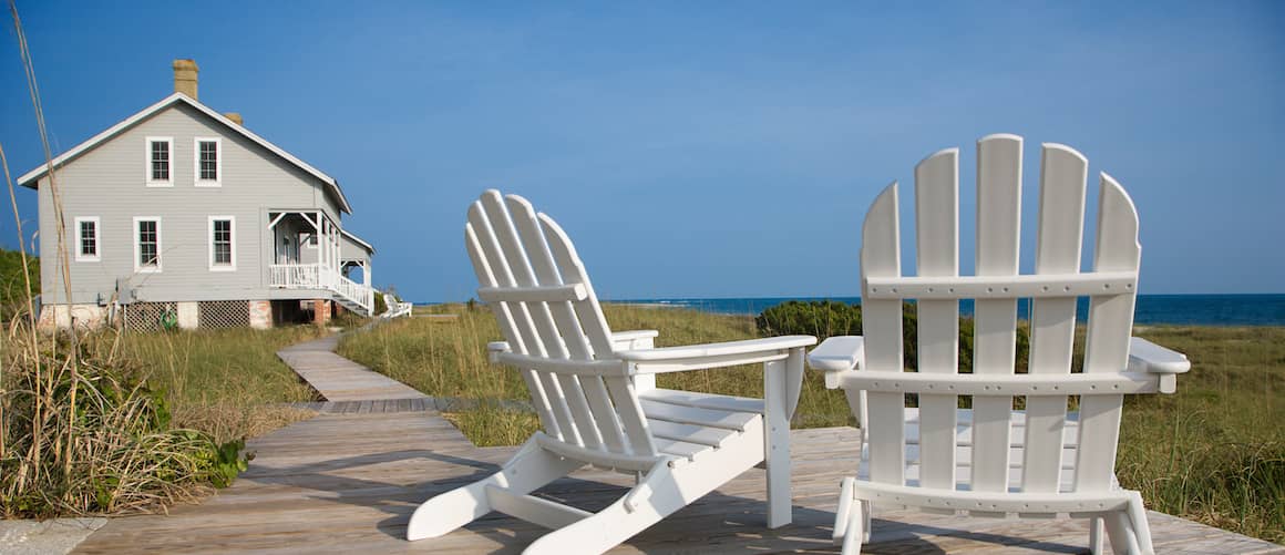 Two beach chairs on boardwalk near vacation home.
