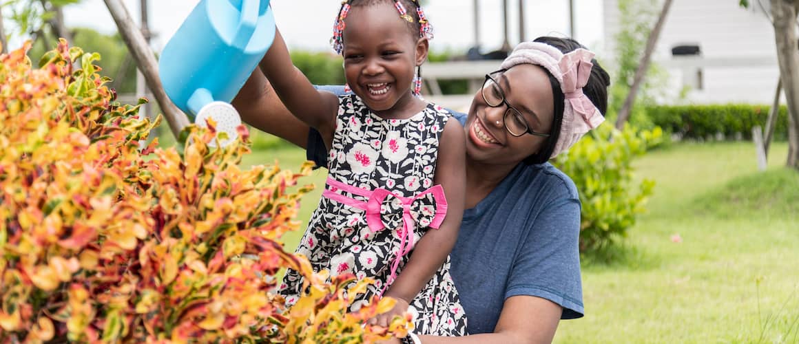 Mother and daughter watering large colorful bush.