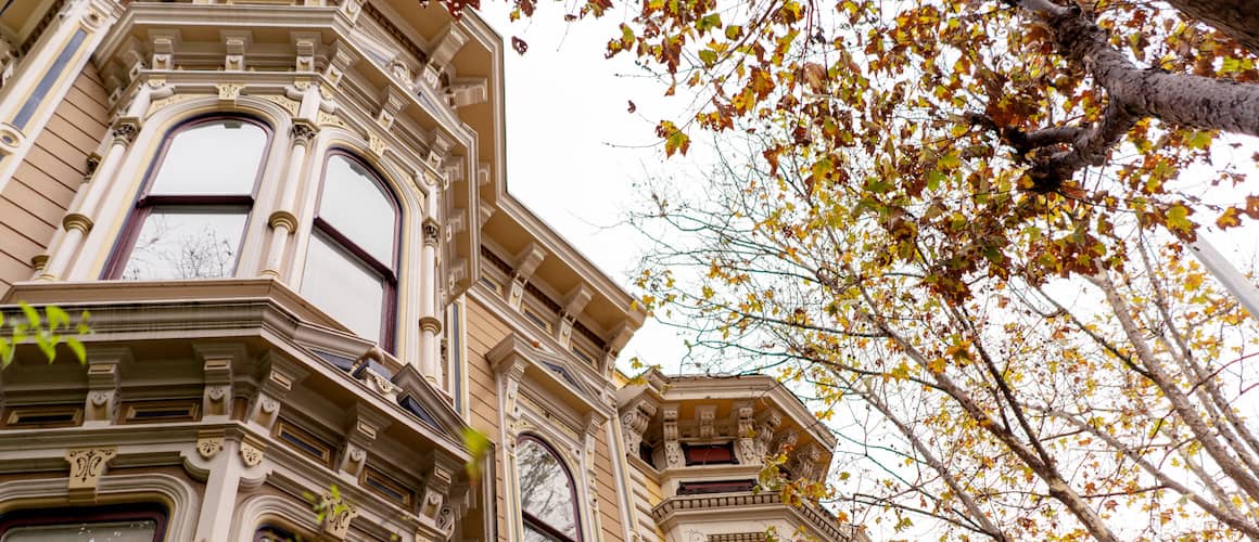 Upper half of a tan victorian style home with bay windows.