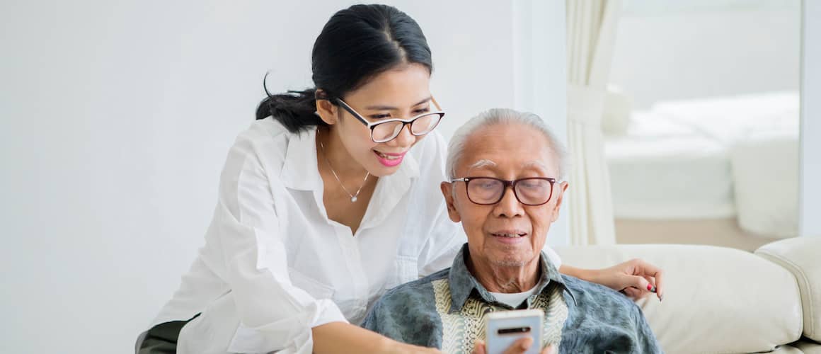Young Asian woman helps her father examine refinance options on smartphone.