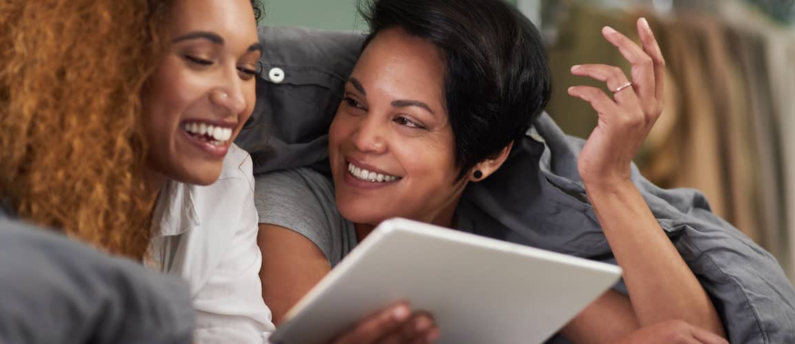 Young lesbian couple looking at a tablet together while in bed.