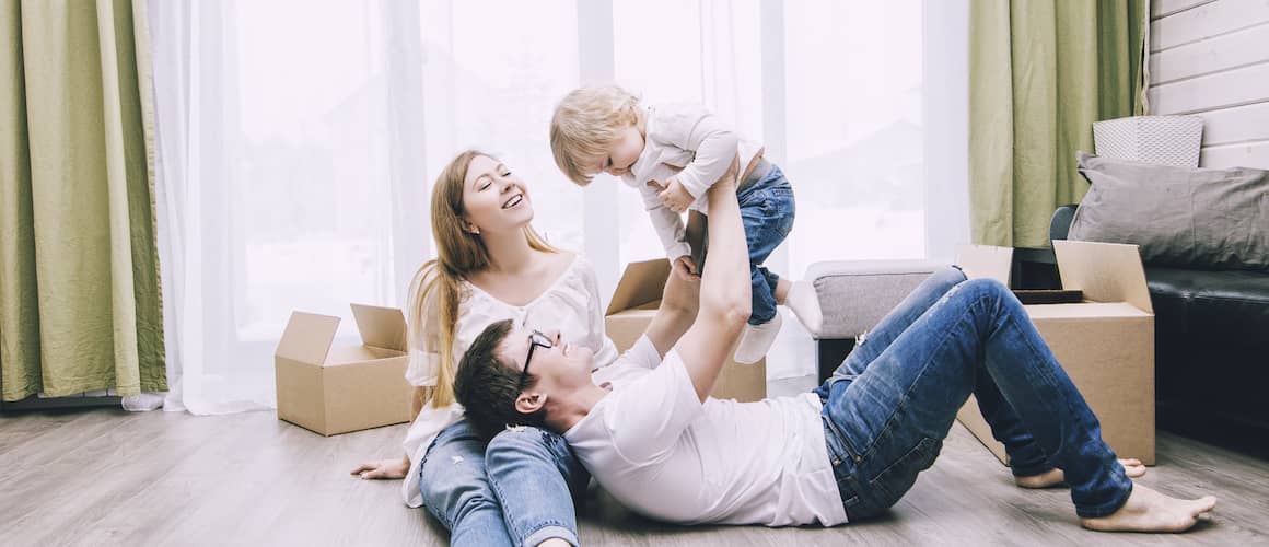 Young Happy Family With A Little Baby And Boxes In New Home
