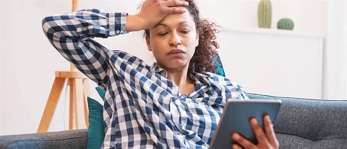 Woman with hand to forehead on couch.