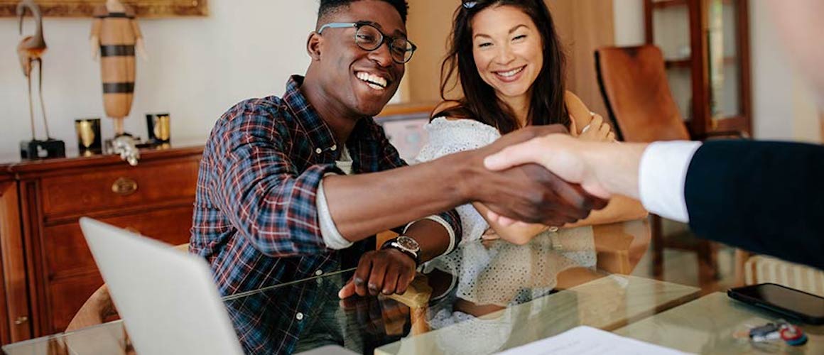 Smiling couple shaking hands with realtor.