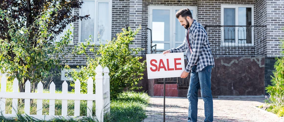 Man staking a SALE sign in front yard of house.