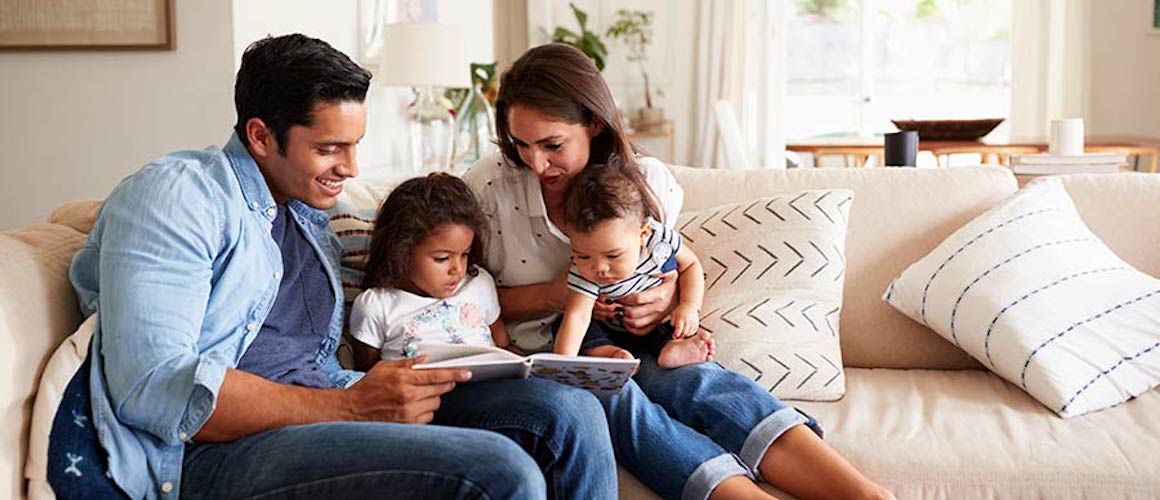 Family with young daughter reading together on couch.