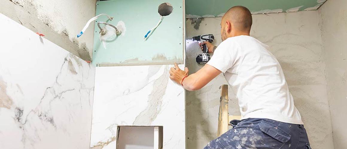 Man on ladder with drill remodeling walls.