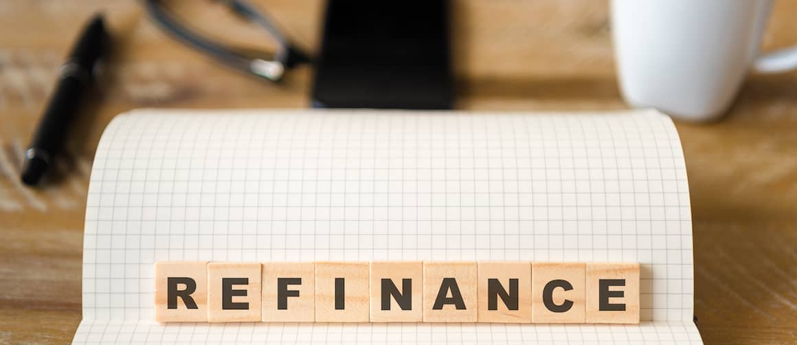 Scrabble letters spelling out REFINANCE on a desk next to coffee cup and reading glasses.