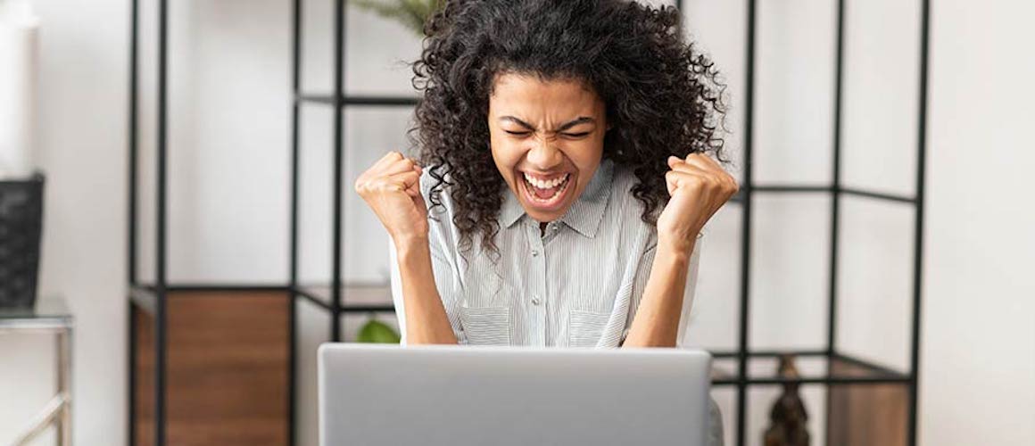 Excited young woman making joyful expression in front of open laptop.