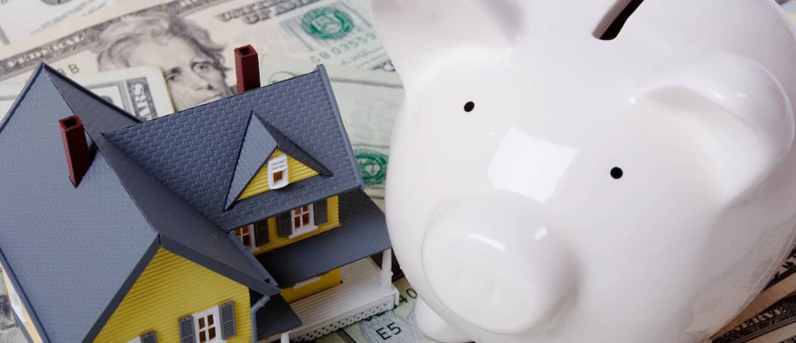 Piggy bank and model of a home with twenty dollar bills spread out around them.